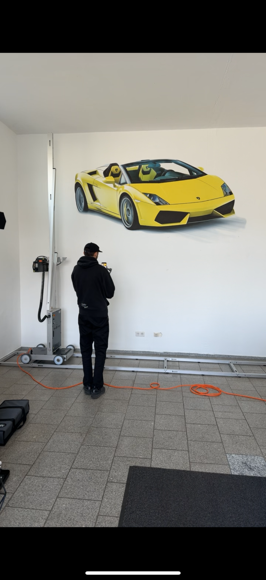 Mann betrachtet gelbes Sportauto auf Wandgemälde in einem Autohaus.