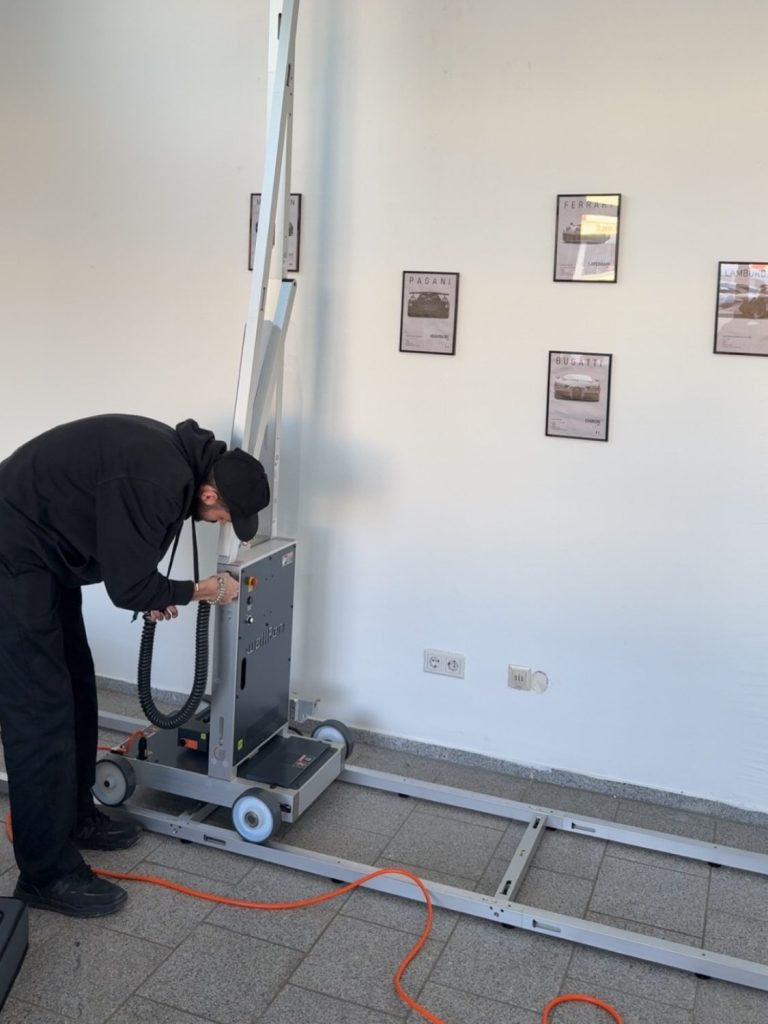 Aufbau des Wanddrucker Eine Person arbeitet an einem Gerät auf einem mobilen Gestell in einem Ausstellungsraum.