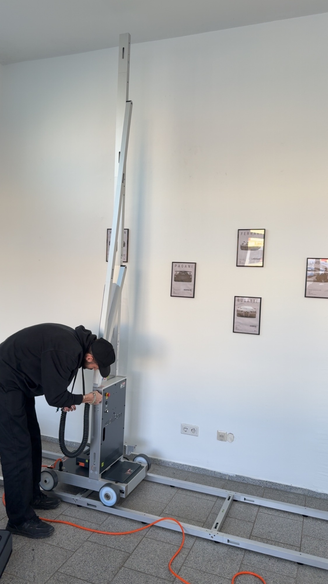 Eine Person arbeitet an einem Aufzugsystem in einem Innenraum mit Bildern an der Wand.