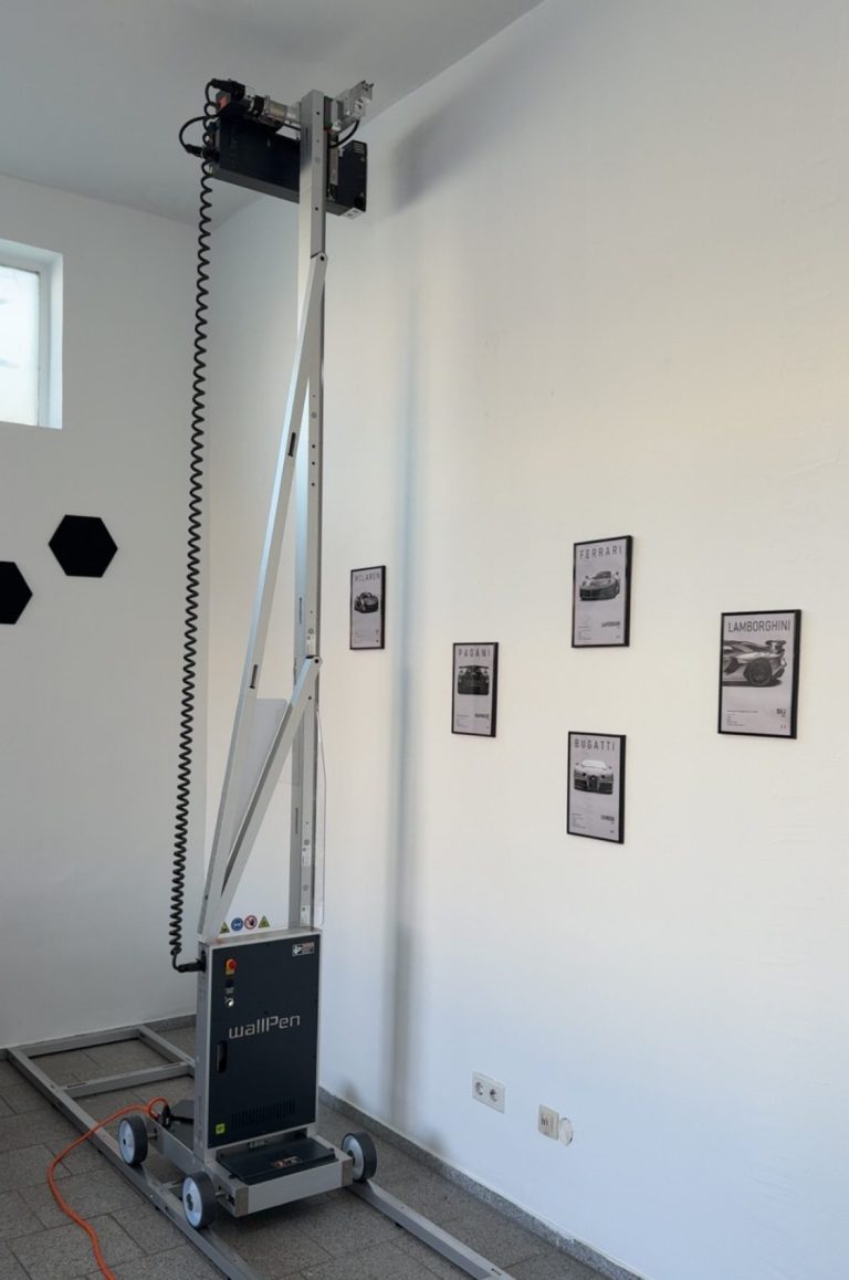 Start des Drucks Ein beweglicher Wanddrucker steht an einer Wand mit mehreren Bildern.